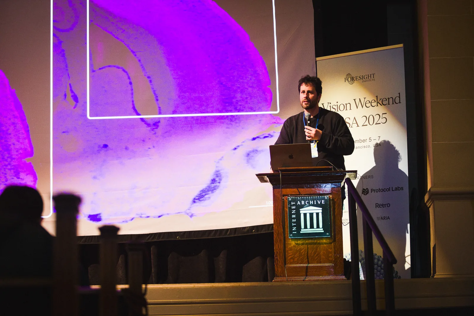 A speaker at a lectern under purple light